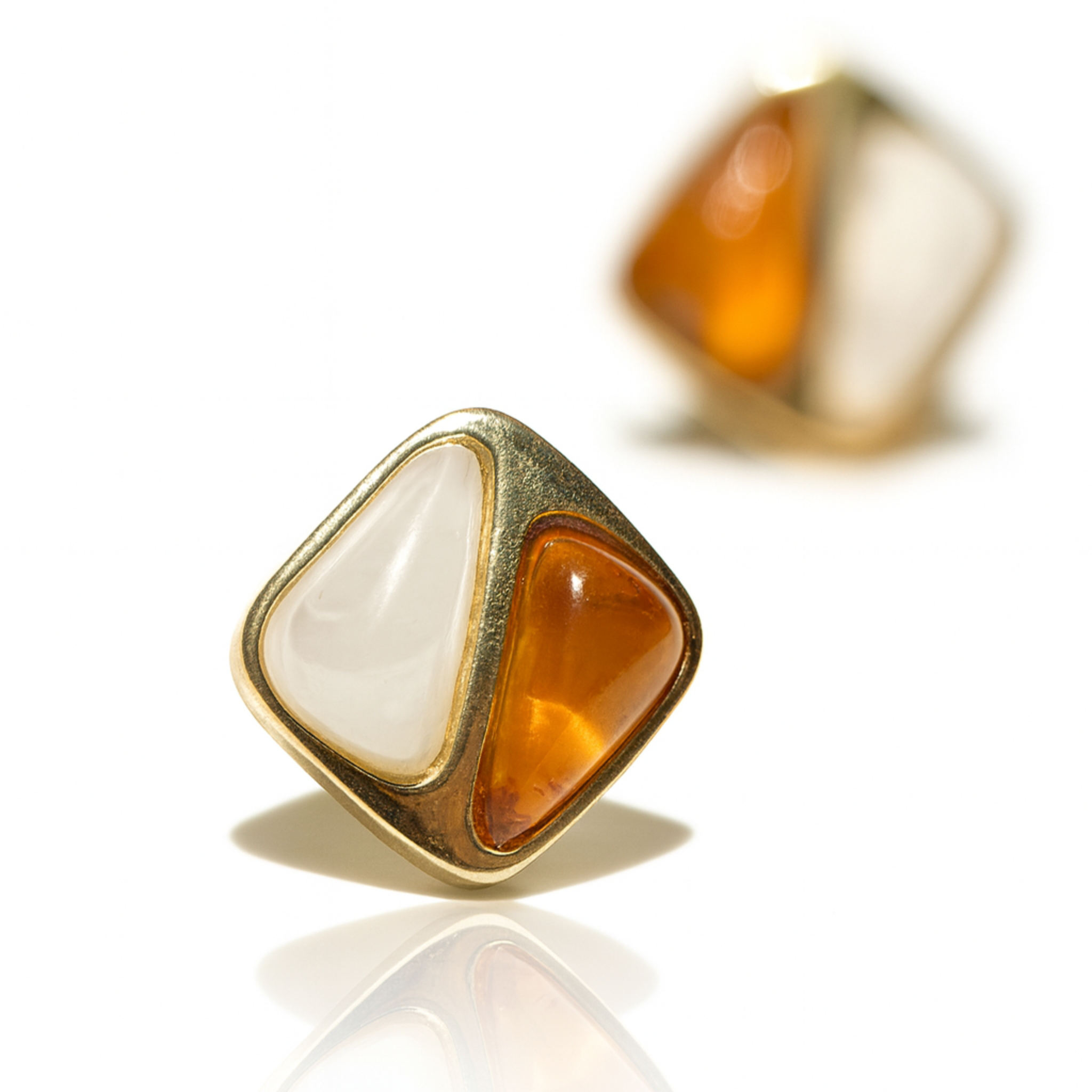 Gold-framed earrings with orange and white stones on a reflective surface.