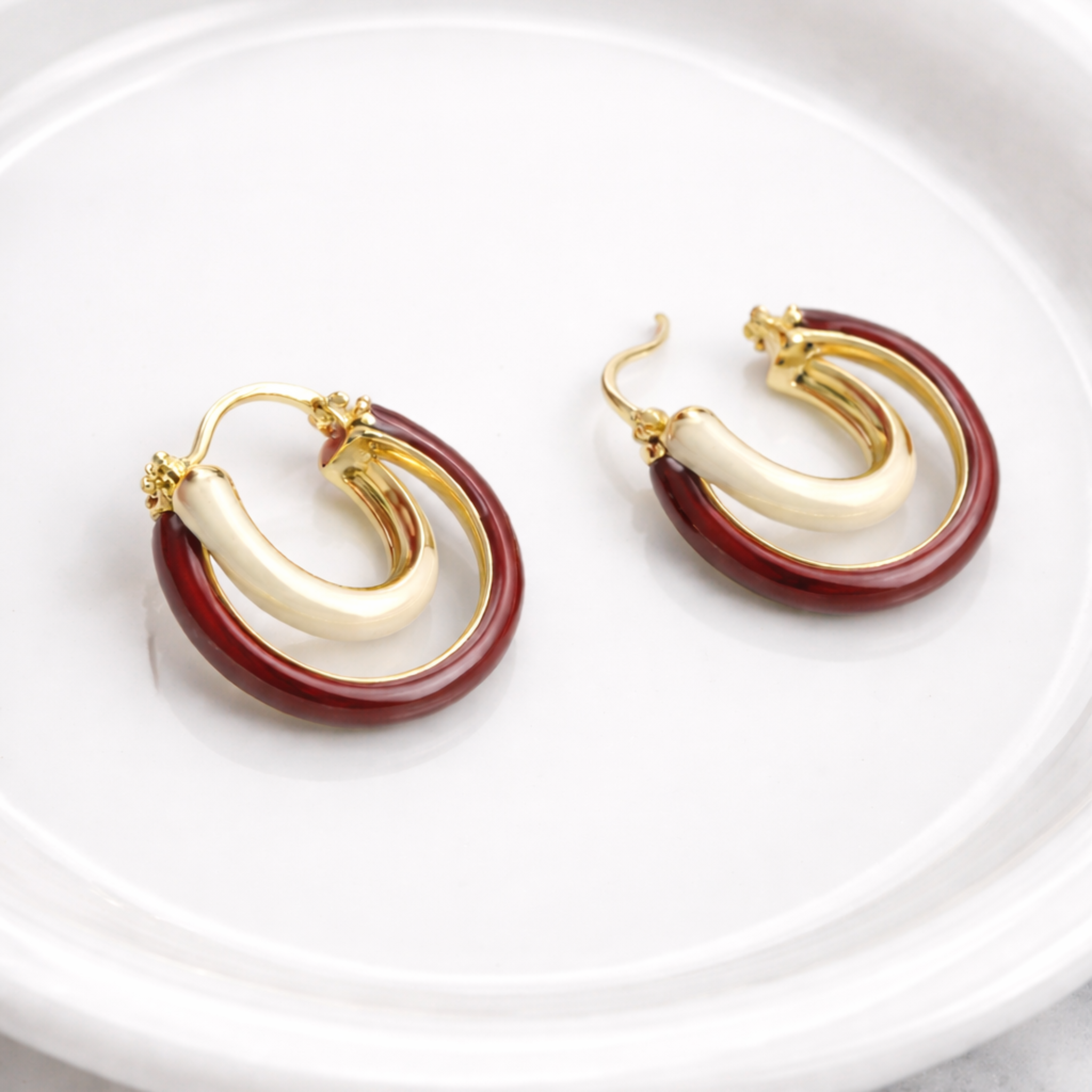 Pair of gold and red hoop earrings on a white plate with a marble background
