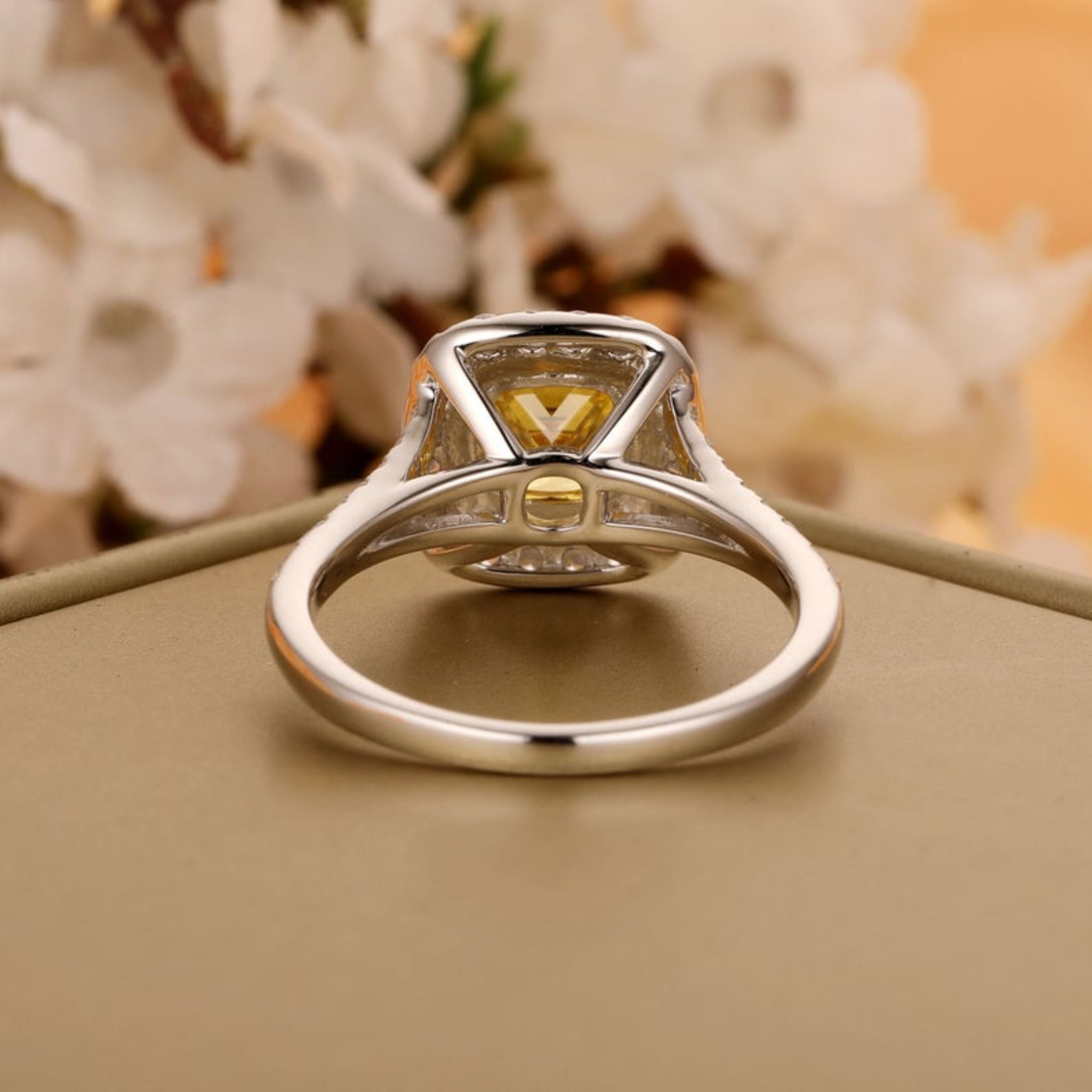 Silver ring with a yellow gemstone on a beige surface with a blurred floral background